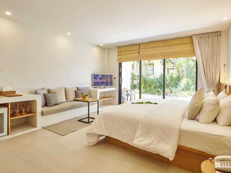 Jasna sypialnia z dużym łóżkiem, beżowym dywanem i tarasem z widokiem na ogród.