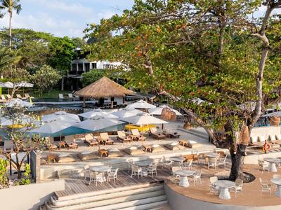 Espace piscine d'hôtel avec transats, parasols et végétation tropicale