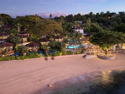 Station balnéaire avec bungalows, piscine et végétation tropicale au coucher du soleil.