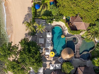 Vue aérienne d'une plage avec piscine, parasols et végétation tropicale dans un complexe.