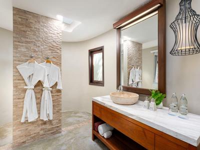 Salle de bain moderne avec meuble en bois, lavabo ovale et deux peignoirs suspendus au mur.