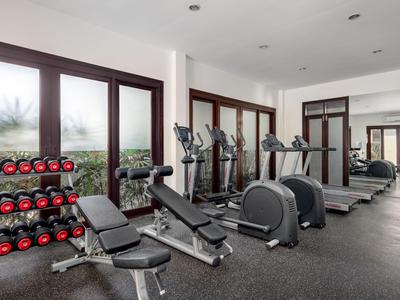 Salle de sport moderne avec haltères, bancs d'entraînement et appareils cardio près de grandes fenêtres.