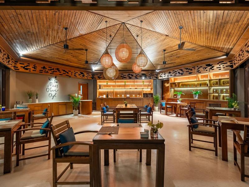 Salle à manger d'hôtel confortable avec plafond en bois, tables et chaises sous une lumière chaude.