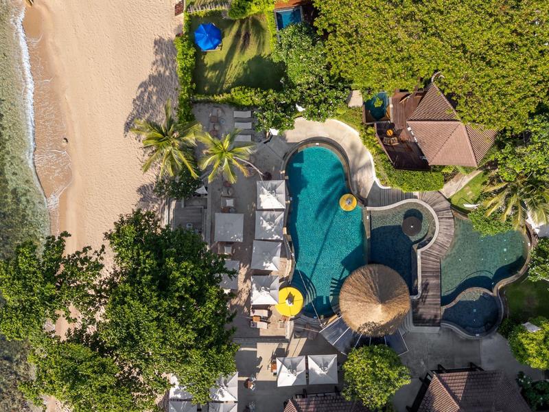 Vue aérienne d'une plage avec piscine, parasols et végétation tropicale dans un complexe.
