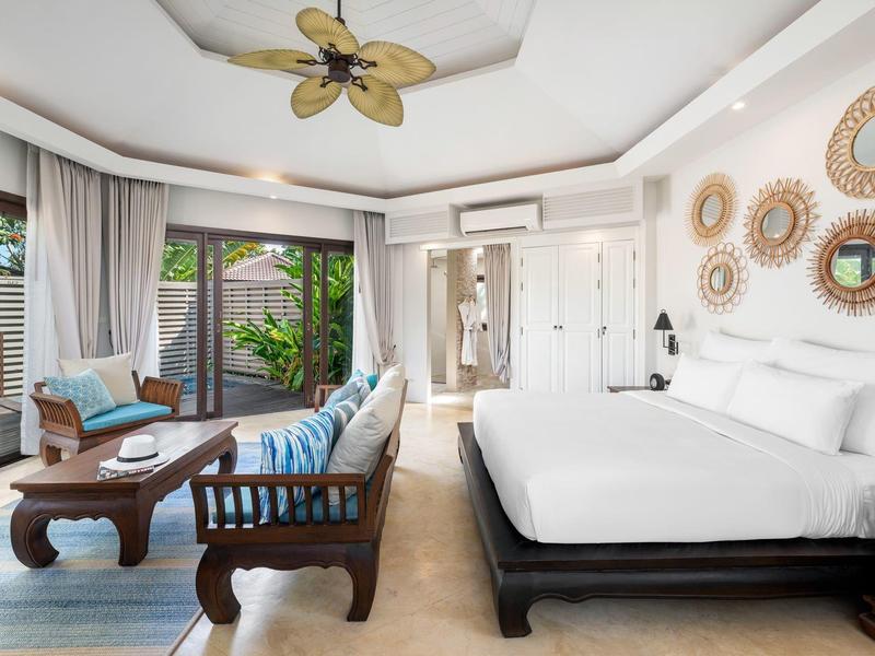 Chambre d'hôtel lumineuse avec grand lit, mobilier en bois, canapé et accès à la terrasse.