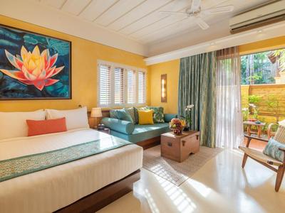 Helles Hotelzimmer mit Doppelbett, Sitzbereich und Zugang zu Terrasse mit Gartenblick.