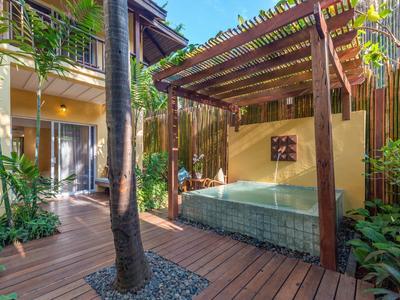 Accogliente area benessere con jacuzzi sotto pergolato in legno circondato da piante tropicali rigogliose.