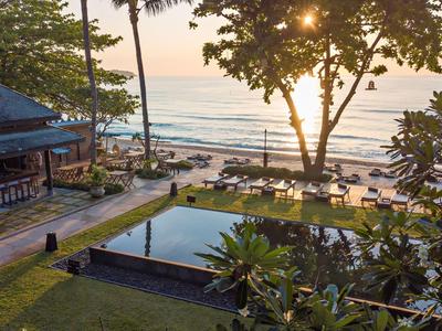 Sonnenuntergang über einem Hotelpool mit Liegestühlen und Meerblick.