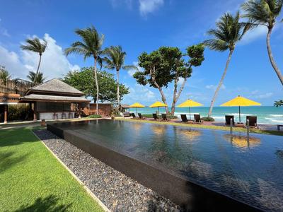 Infinity-Pool am Meer mit Palmen, Sonnenschirmen und einer Lounge-Bar an der Seite.