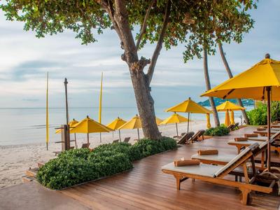 Strand mit Liegestühlen, Sonnenschirmen und Baum neben Holzsteg am Meer