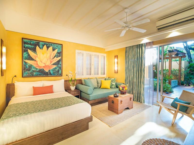 Camera d'hotel luminosa con letto matrimoniale, divano, quadro e accesso diretto alla terrazza.