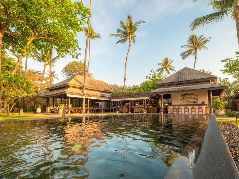 Resort con bungalow tradizionali e giardino di palme accanto a una piscina al tramonto.