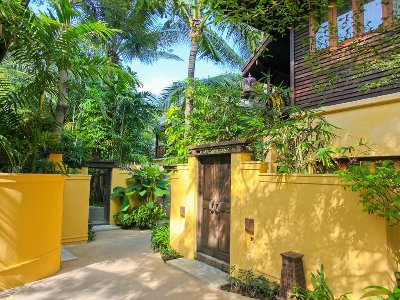 Ingresso di una casa vacanze tropicale con pareti gialle e rigogliosa vegetazione verde.