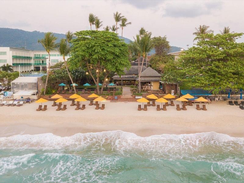 Spiaggia con ombrelloni gialli, alberi verdi e un edificio dell'hotel sullo sfondo.