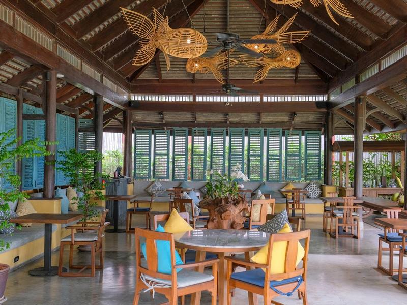 Area lounge aperta dell'hotel con mobili in legno e sculture decorative di pesci sotto il tetto.