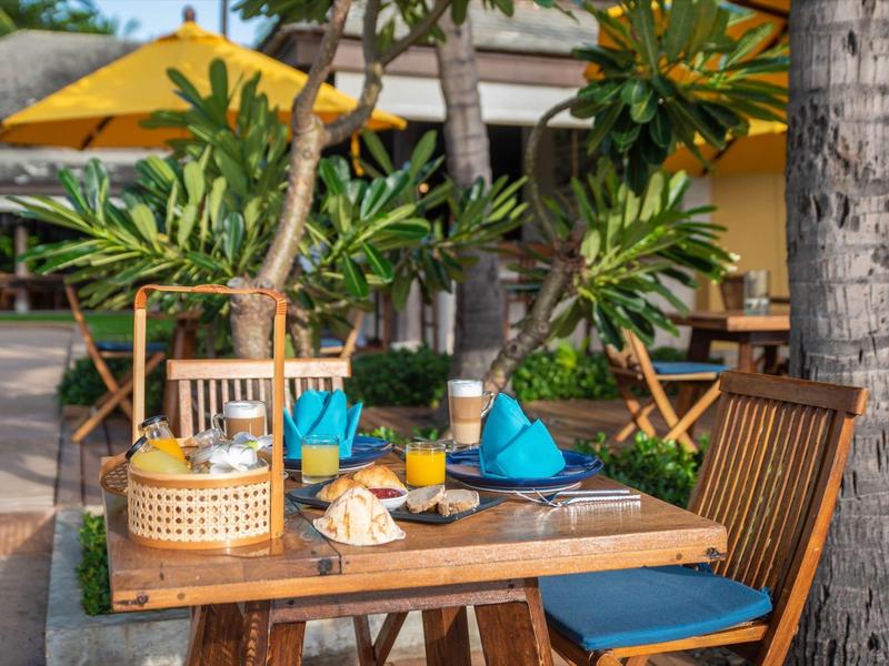 Un tavolo apparecchiato con tovaglioli blu e un cestino da picnic all'aperto accanto alle palme.