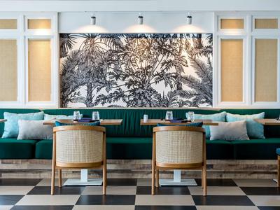 Elegantní hotelová lounge s zelenou čalouněnou lavicí, dřevěnými stoly a černobílým obrazem na stěně.