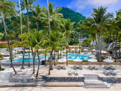 Blick auf einen tropischen Poolbereich mit Palmen und Liegestühlen vor einem grünen Berg.