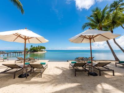 Strandhotel mit Liegestühlen, Sonnenschirmen und Palmen am klaren blauen Meer.