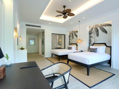 Světle hotelový pokoj se dvěma postelemi, stropním ventilátorem a moderním stolem.