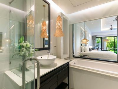 Moderní koupelna se umyvadlem, velkým zrcadlem a skleněnou sprchou v hotelovém pokoji.