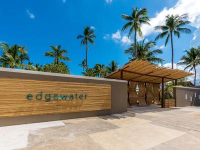 Moderner Hoteleingang mit Holzwand, Schriftzug und Palmen unter klarem blauem Himmel.