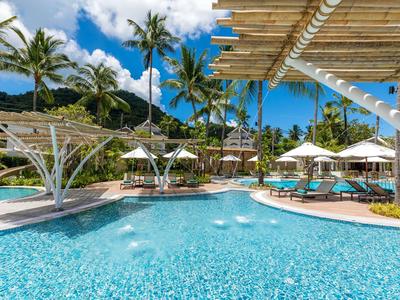 Poolbereich in tropischem Resort mit Palmen, Liegestühlen und Sonnenschirmen an sonnigem Tag