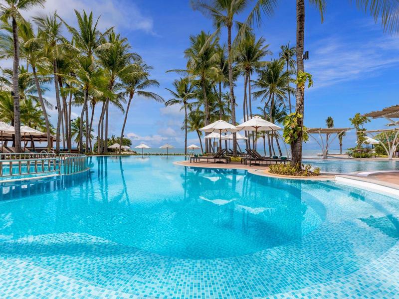 Velký tropický bazén s palmami, slunečníky a jasnou oblohou v letovisku