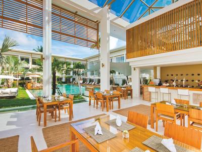 Nowoczesna, otwarta restauracja z drewnianymi meblami i widokiem na basen i ogród.