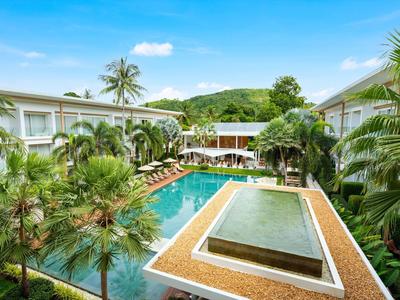Complejo hotelero con gran piscina, tumbonas y palmeras bajo un cielo azul.