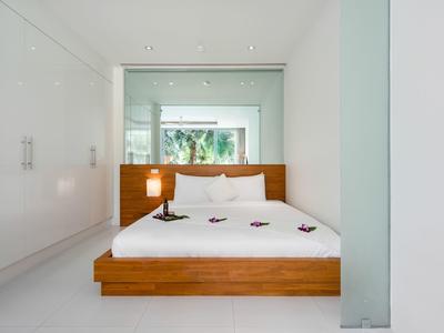 Dormitorio minimalista con cama blanca y marco de madera en una habitación moderna y luminosa.