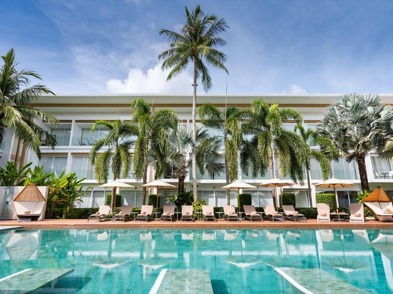 Piscina moderna de hotel con tumbonas y palmeras bajo un cielo azul.