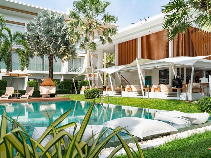 Piscina moderna de hotel con tumbonas, jardín de palmeras y zona de descanso a la luz del día.