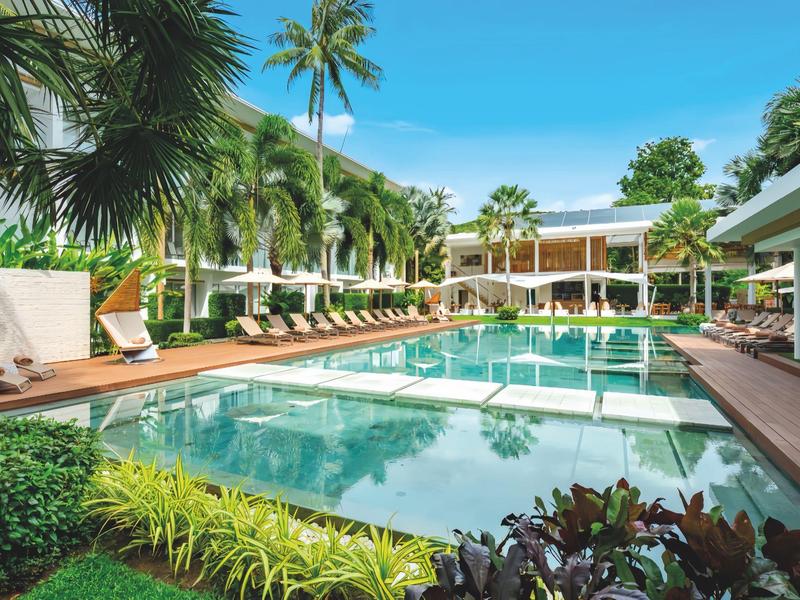 Piscina moderna de hotel con tumbonas y palmeras bajo un cielo azul.