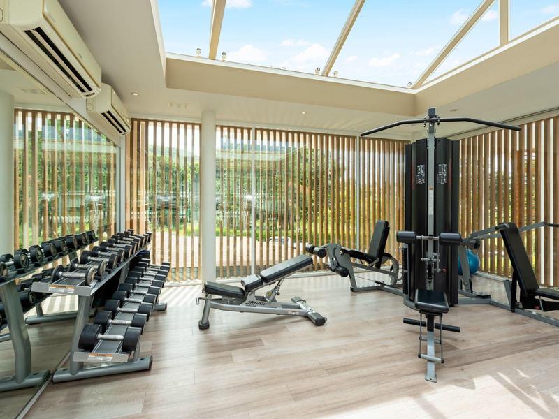 Gimnasio luminoso con pesas, máquinas de ejercicio y techo de vidrio para luz natural.