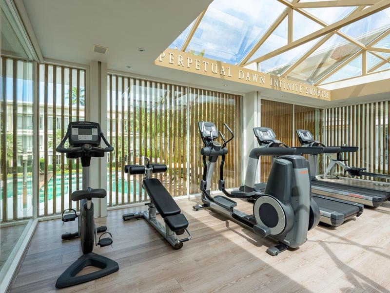 Gimnasio moderno con cintas de correr, bicicletas y elípticas junto a grandes ventanas.