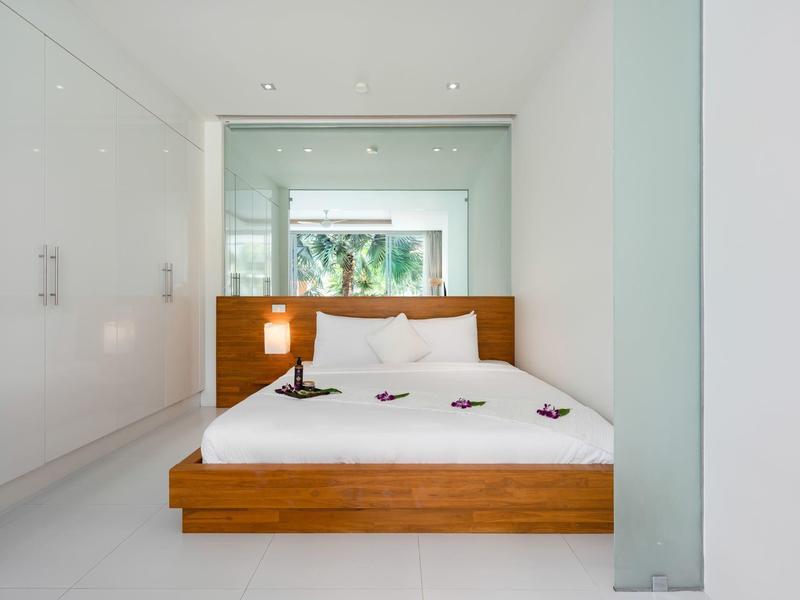 Dormitorio minimalista con cama blanca y marco de madera en una habitación moderna y luminosa.