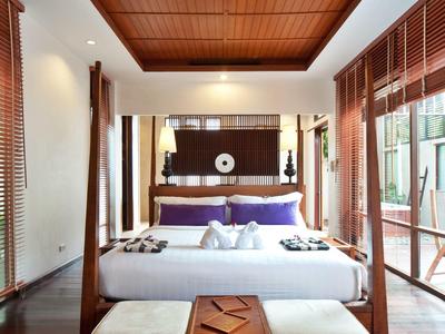 Chambre d'hôtel élégante avec lit king-size, sol en bois et grandes fenêtres avec stores.