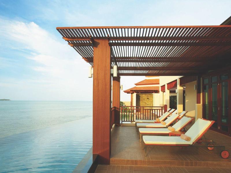Terrasse avec chaises longues au bord de l'eau sous un ciel bleu avec des nuages.