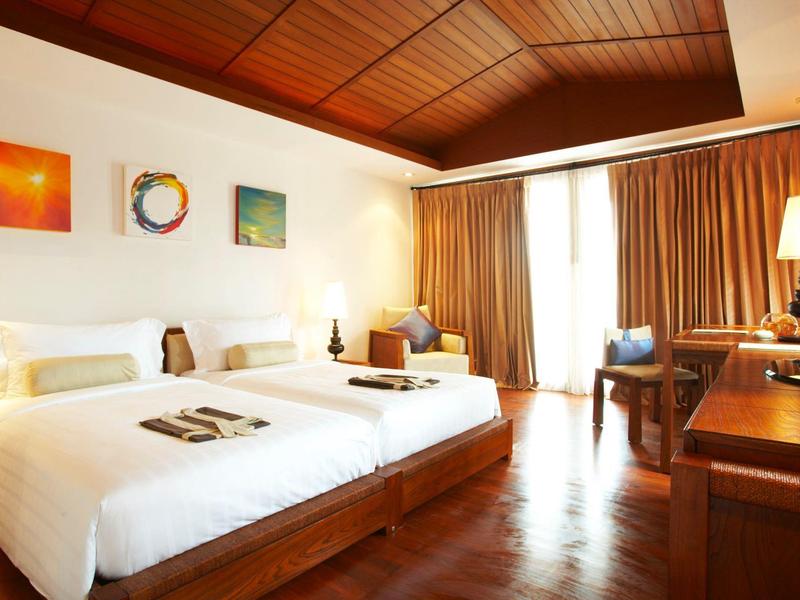 Chambre d'hôtel avec deux lits jumeaux, plafond en bois et grandes fenêtres avec rideaux.