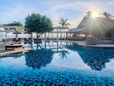 Hotelpool mit Sonnenliegen, Palmen und Blick auf das Meer bei Sonnenuntergang.
