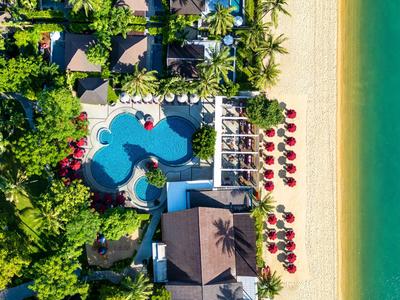 Luftaufnahme eines Resorts mit Pool, Strand und roten Sonnenschirmen entlang des Sandes.