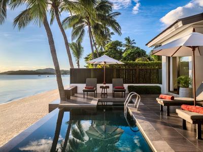 Luxuriöser Poolbereich mit Liegestühlen, Sonnenschirm und Palmen am Strand bei Sonnenuntergang.