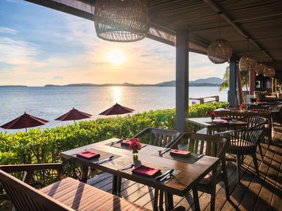 Außenrestaurant mit Tischen und Stühlen am Meer bei Sonnenuntergang.