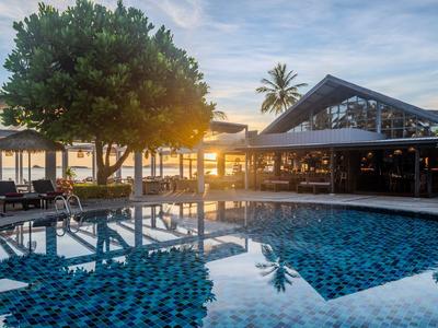 Blick auf einen Pool mit Sonnenuntergang, umgeben von Bäumen und einem Hotelgebäude.