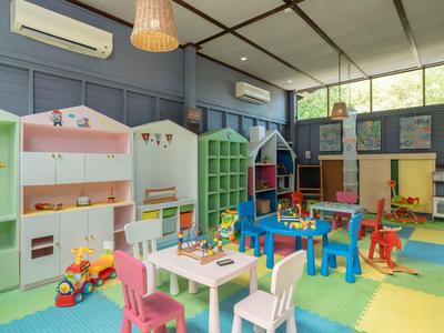 Sala de juegos infantil colorida con juguetes, mesas, sillas y suelo de espuma brillante.