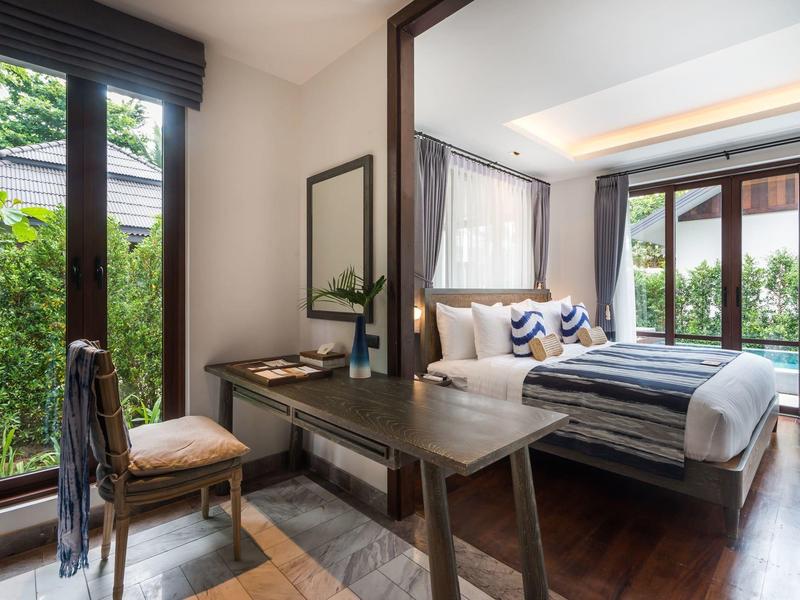 Helles Hotelzimmer mit Holzschreibtisch, Stuhl und Blick auf das Bett und den Garten.