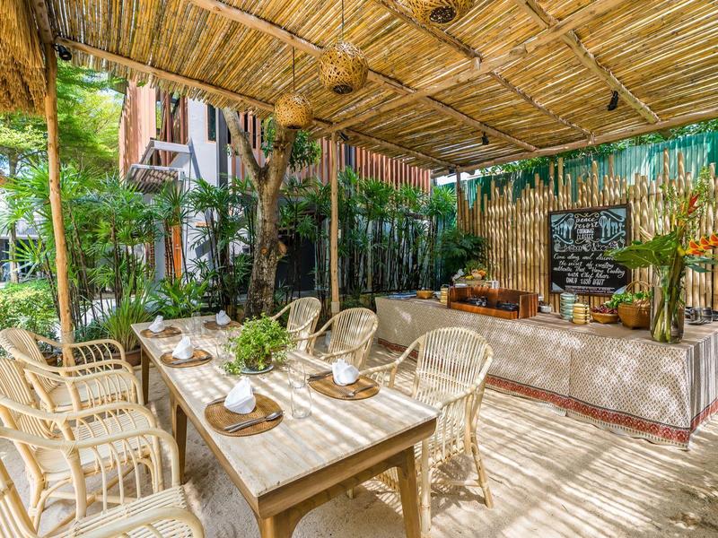 Gemütlicher überdachter Außenbereich mit Holzmöbeln und grüner Dekoration in einer Hotelumgebung.