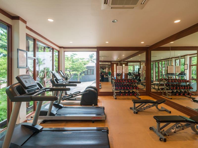 Helles Fitnessstudio mit Laufbändern, Hanteln und großen Fenstern mit Blick ins Grüne.