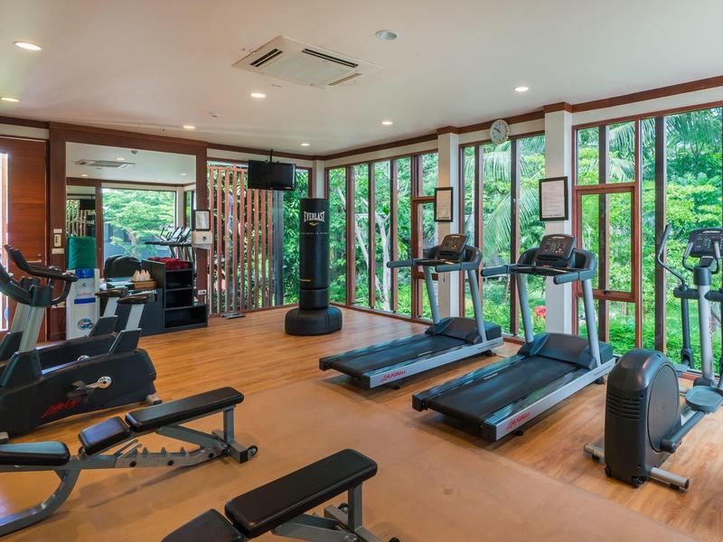 Heller Fitnessraum mit Laufbändern, Fahrradergometern und großen Fenstern mit Blick auf grüne Natur.